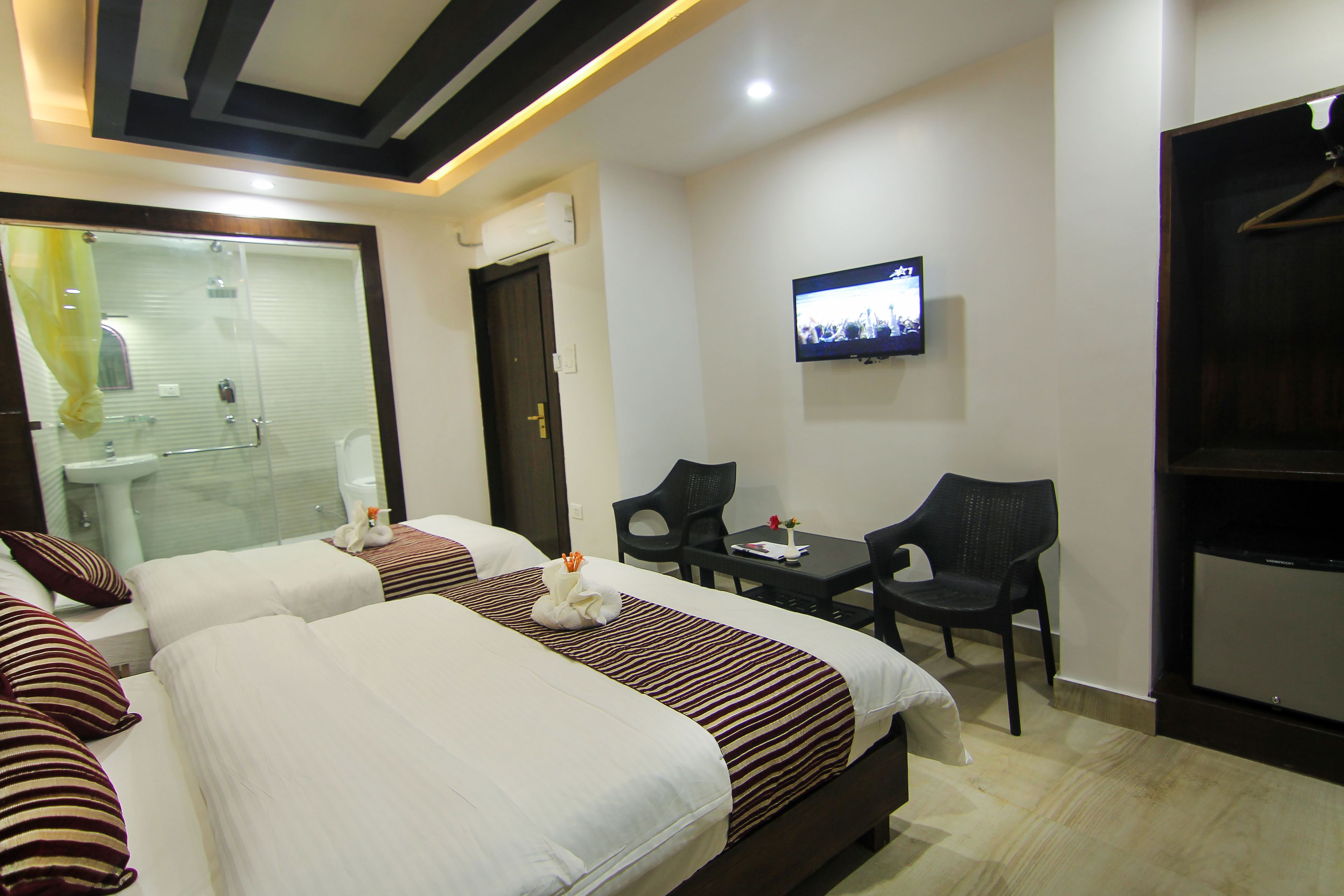A hotel room with two beds, a desk, a TV, and a shower area.