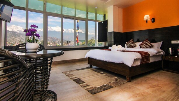 A modern hotel room with a large bed, a view of mountains, a dining area with a table and chairs, and a TV on the wall. - Hotel Lakeside (Pokhara)