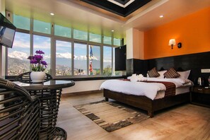 A modern hotel room with a large bed, a view of mountains, a dining area with a table and chairs, and a TV on the wall. - Hotel Lakeside (Pokhara)
