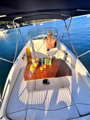 A boat deck with a table set for drinks, a person seated at the back, and a view of the sea and boats in the background. - Above the Blue: 1BR Peaceful Horizon Pool&Terrace (Bosanka)