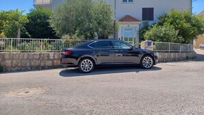 A black car parked in front of a two-story building with a tiled roof and a white fence. - Above the Blue: 1BR Peaceful Horizon Pool&Terrace (Bosanka)