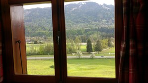 A window with a view of a green landscape, a road, and a forested hill.