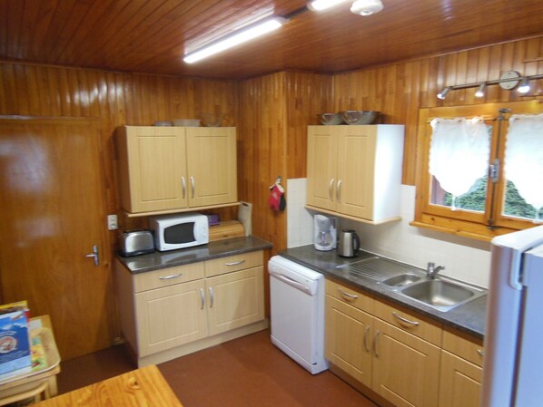 A compact kitchen with wooden cabinets, a microwave, a dishwasher, and a sink. - Large Family Friendly Chalet With Panoramic Mountain Views (Samoëns)