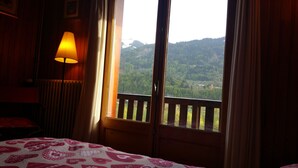 A room with a bed, a lamp, and a window with a view of a forested mountain.