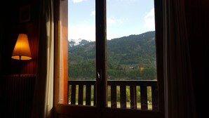 A room with a view of a mountainous landscape through a window with a wooden railing.