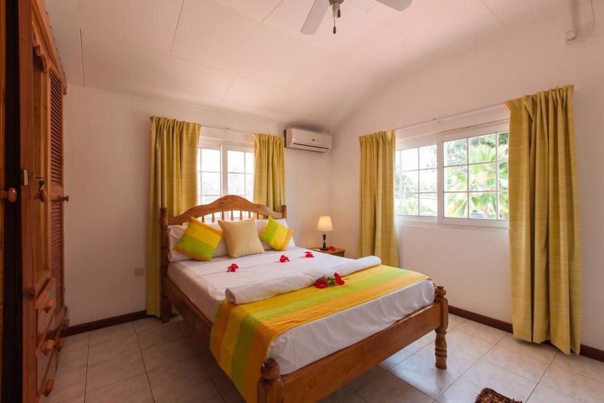 A bedroom with a wooden bed, yellow curtains, a ceiling fan, and an air conditioning unit.