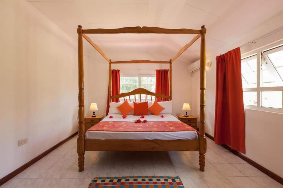 A four-poster bed with a wooden frame, two bedside tables, and red curtains.