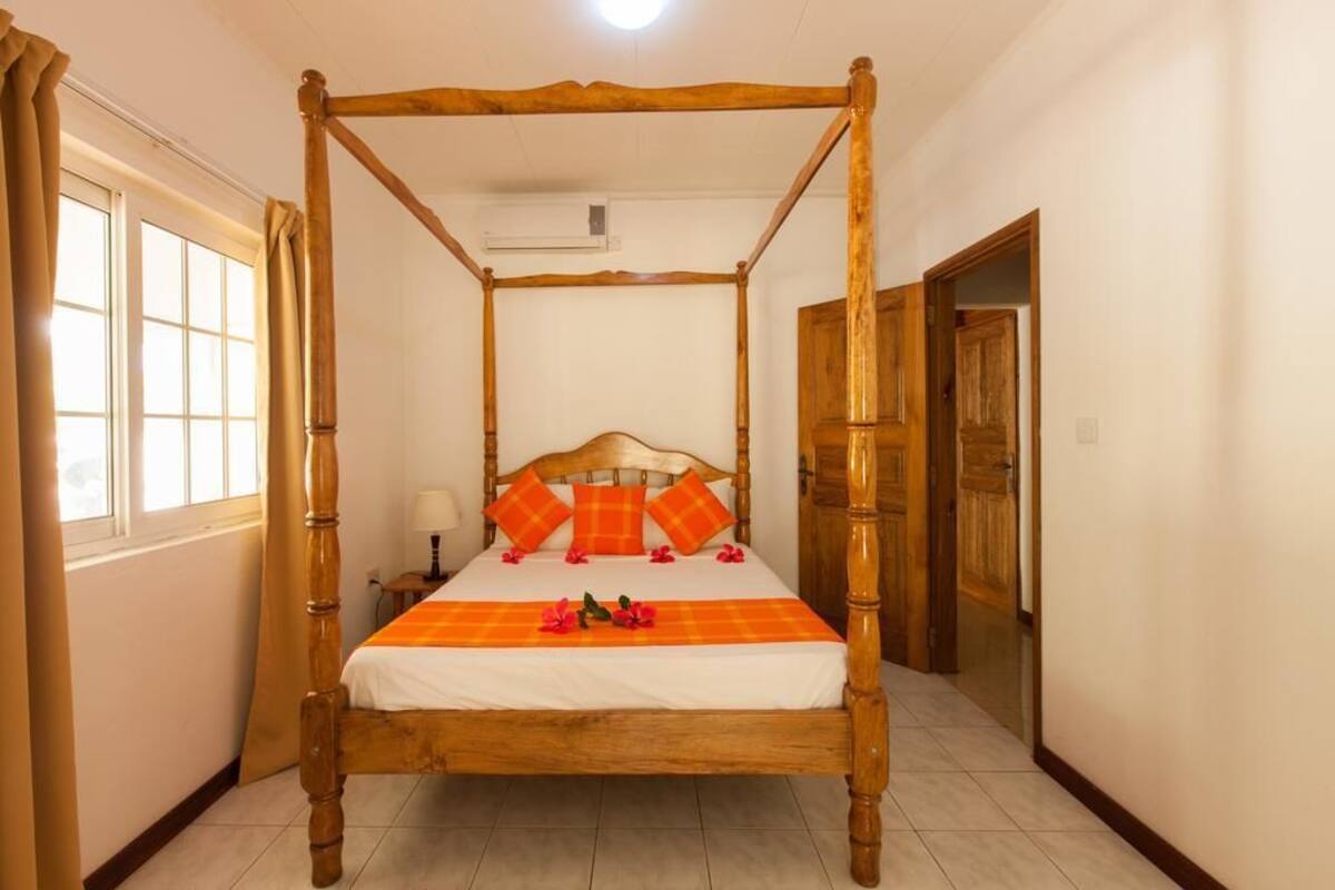 A four-poster bed with a wooden frame, white bedding, and orange pillows.