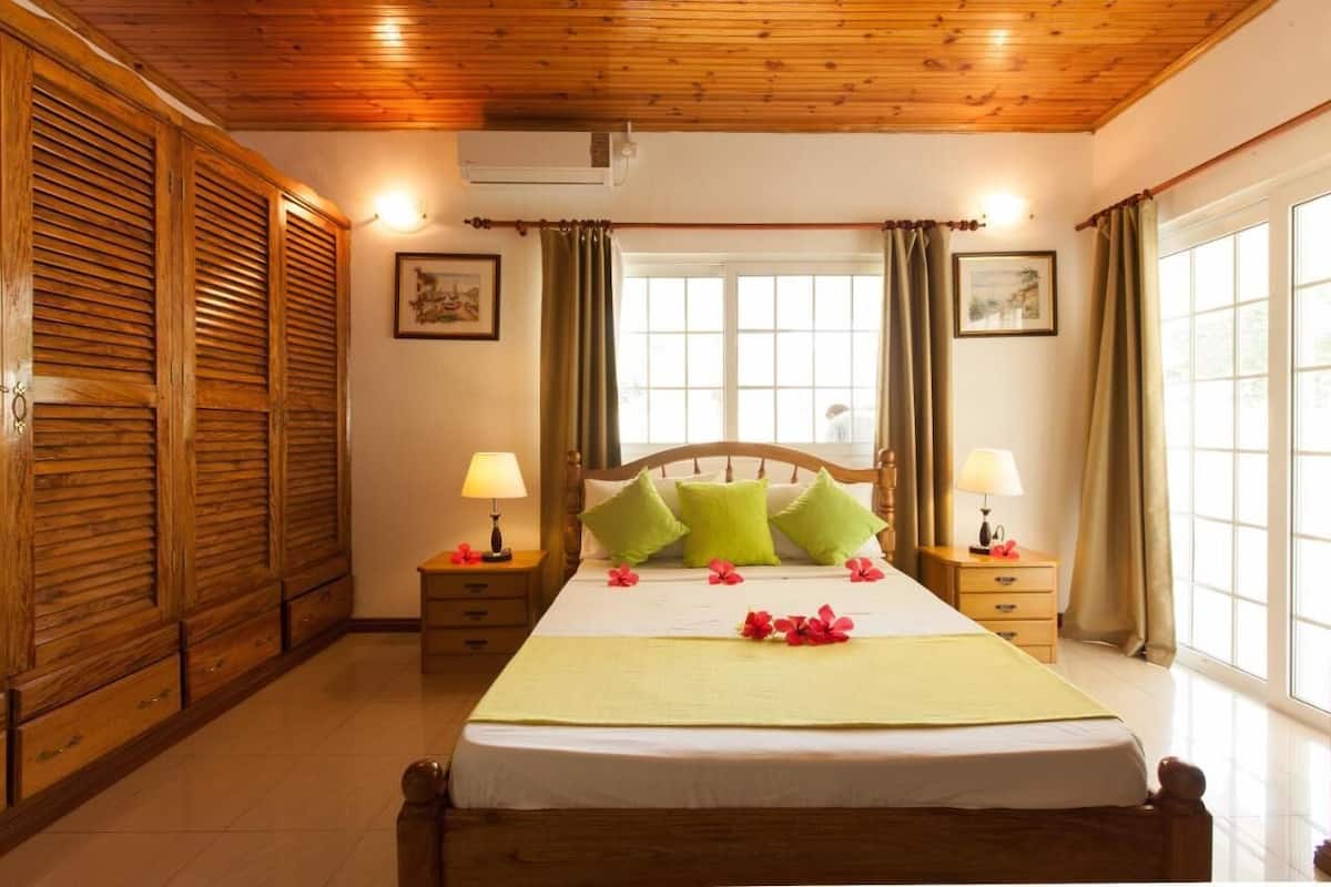A hotel room with a wooden ceiling, a large bed with green pillows, two bedside tables with lamps, and a window with curtains.
