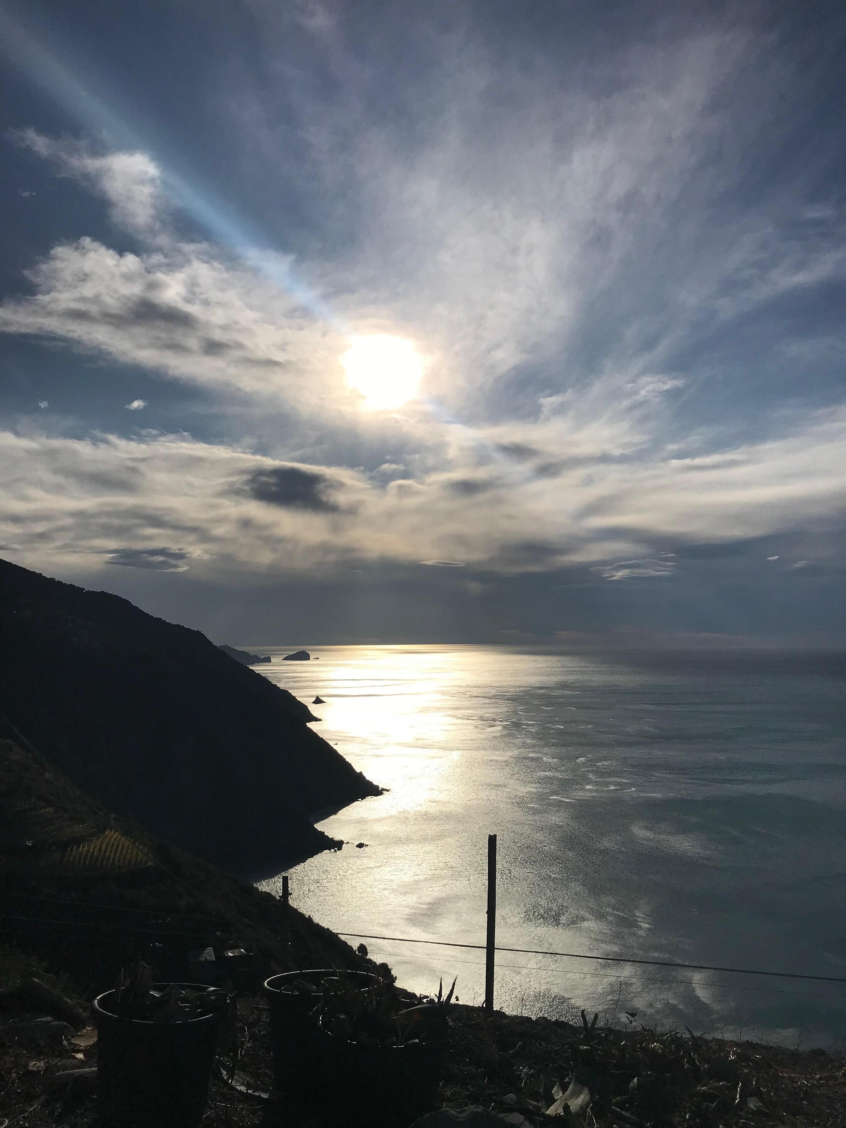 Eine Küstenlandschaft mit Blick auf das Meer und einer entfernten Sonne.
