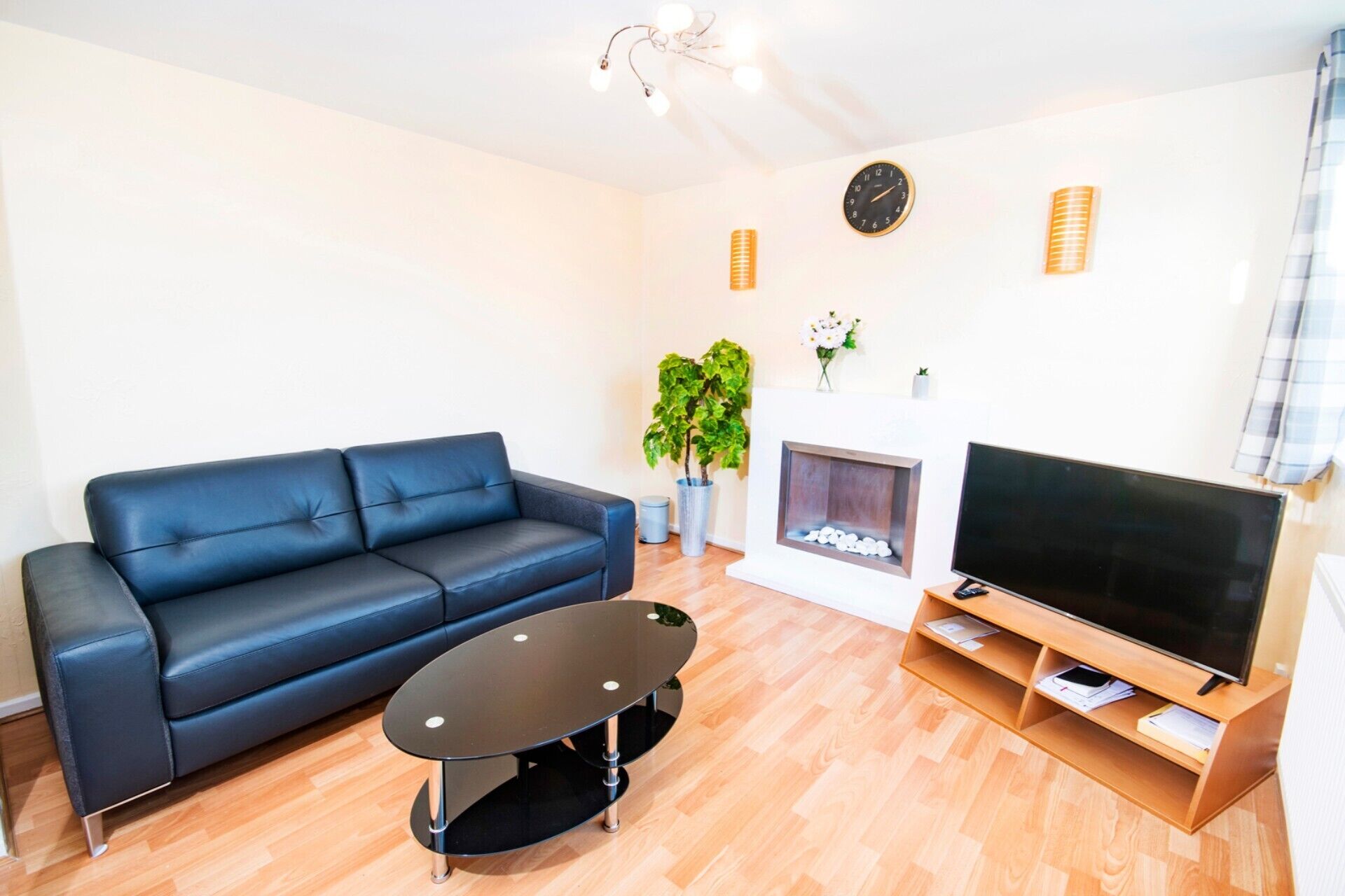 Ein Wohnzimmer mit einem blauen Sofa, einem schwarzen Couchtisch, einem Fernseher auf einem Holzboden, einem Kamin und einer Uhr an der Wand.