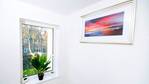 A room with a window overlooking a residential area, a framed painting on the wall, and a potted plant on the windowsill.