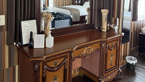 Ein Zimmer mit einem großen Spiegel, einer Holzkommode mit Schubladen, einem Bett und einer Uhr an der Wand.
