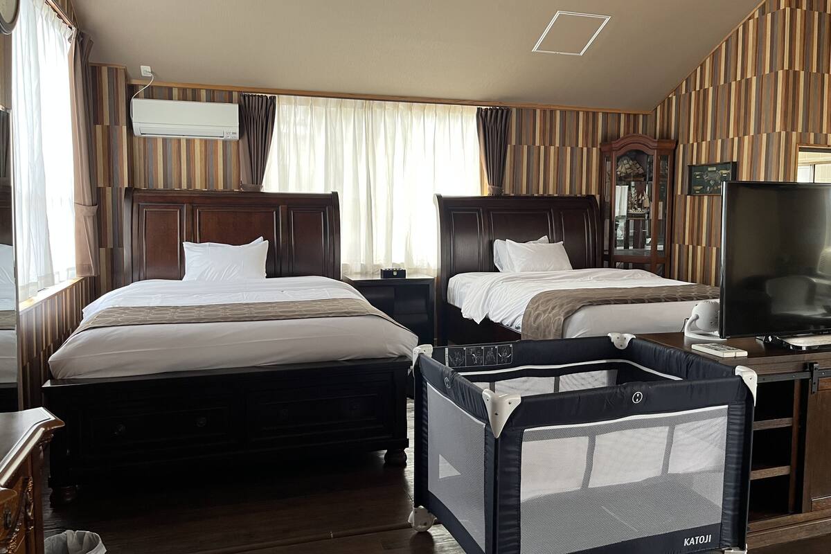 Ein Hotelzimmer mit zwei Betten, einem Fernseher, einem Schreibtisch und einem Reisebett.