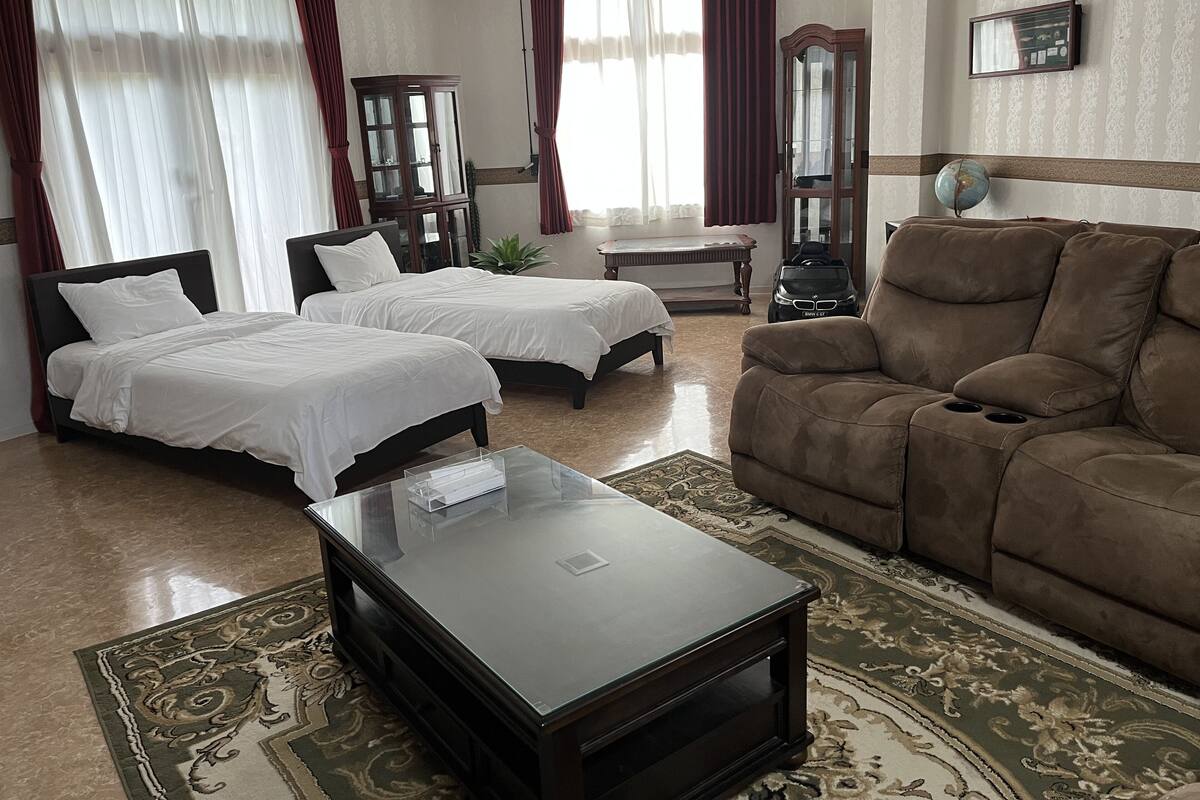 Ein Hotelzimmer mit zwei Betten, einem braunen Sofa, einem Glastisch, einem Schreibtisch und einem Stuhl.