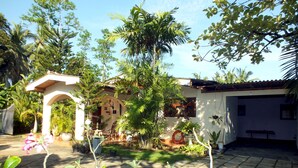 A courtyard with a white building, a stone pathway, and various plants. - River Side Villa (Galle)