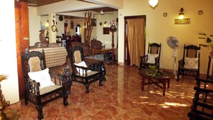 A spacious living room with a high ceiling, wooden beams, and a tiled floor. There are several antique-style chairs and a table with a fan. - River Side Villa (Galle)