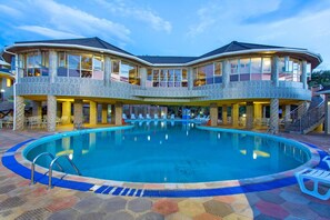 A large indoor swimming pool with a multi-level building structure surrounding it, featuring multiple balconies and a covered patio area. - Nokras Riverine Hotel & Spa (Sagana)
