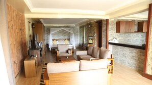 Een ruime woonkamer met een bank, fauteuils, een salontafel en een televisie. Achtergrond is een stenen muur en houten kasten.