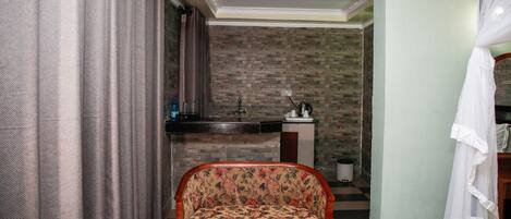Una habitación con sofá, kitchenette pequeño, cortina y cama con dosel.