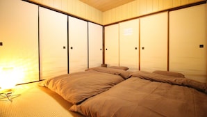 Een traditionele Japanse kamer met schuifdeuren, een bed met bruin beddengoed en een zichtbare lichtbron aan de linkerkant.