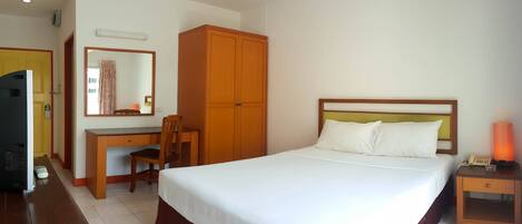 A hotel room with a bed, a desk with a chair, a wardrobe, a bedside table with a lamp, and a television.