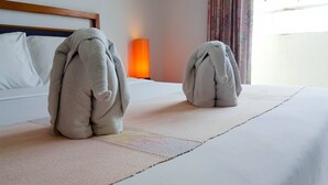 A hotel room with a neatly made bed, a bedside lamp, and a window with curtains. - Eastiny Bella Vista Hotel (Pattaya)