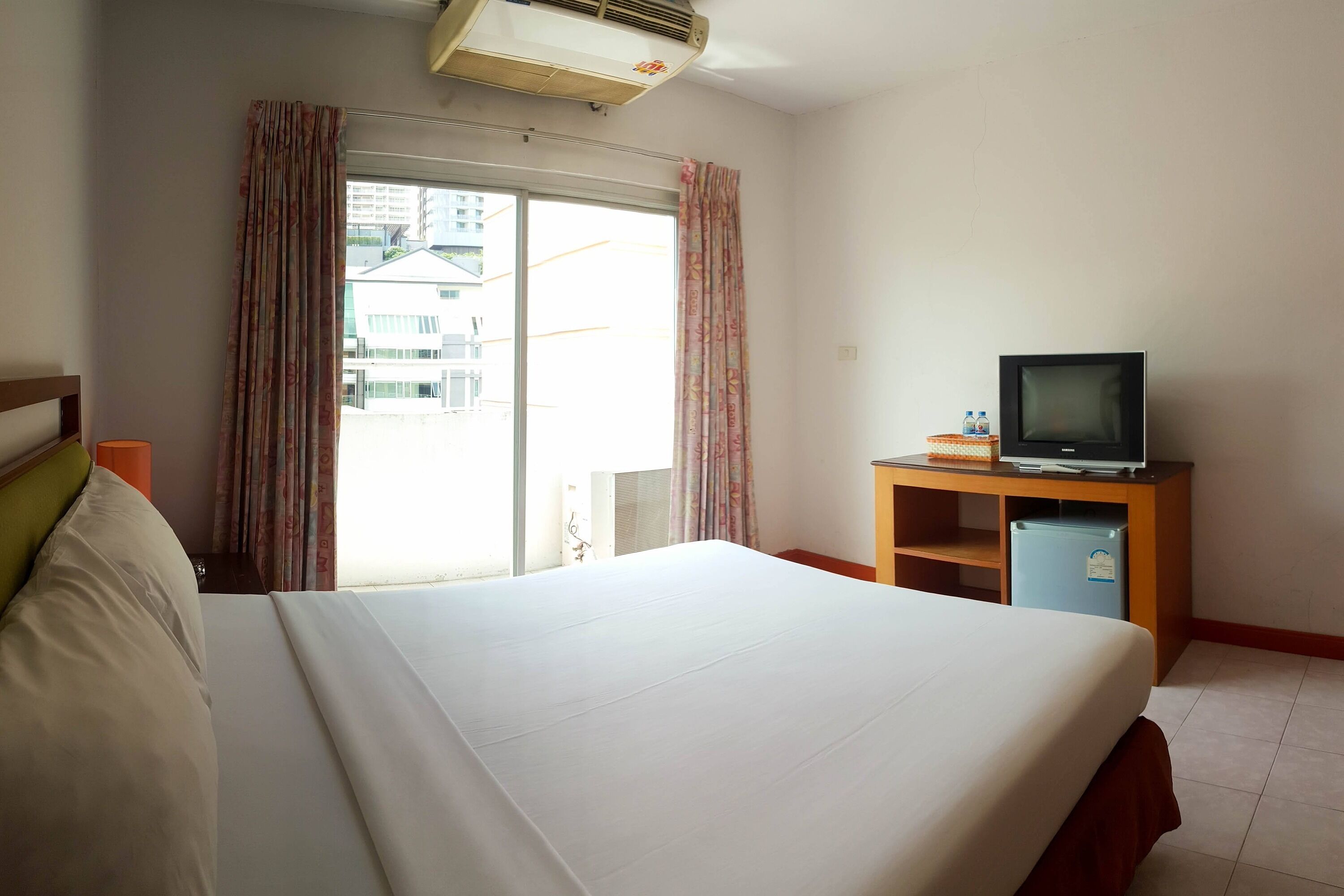 Una habitación de hotel con una cama, un televisor sobre un soporte de madera y una ventana con cortinas.