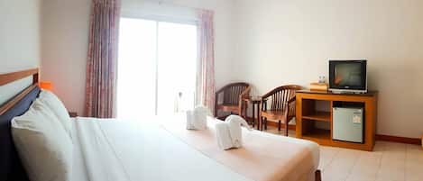 A hotel room with a bed, a desk with a television, a refrigerator, and a chair.