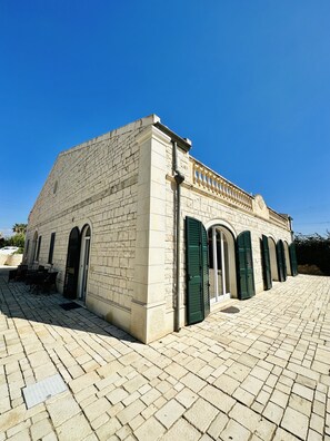 Un edificio de fachada de piedra, ventanas de arco y un patio empedrado.