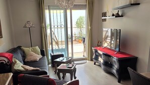 A living room with a sofa, armchair, coffee table, TV stand, and a sliding glass door leading to an outdoor area with potted plants. - Urban Oasis & Private Terrace. (València)
