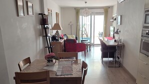 A dining area with a wooden table and chairs, a red sofa, a TV, and an air conditioning unit. - Urban Oasis & Private Terrace. (València)