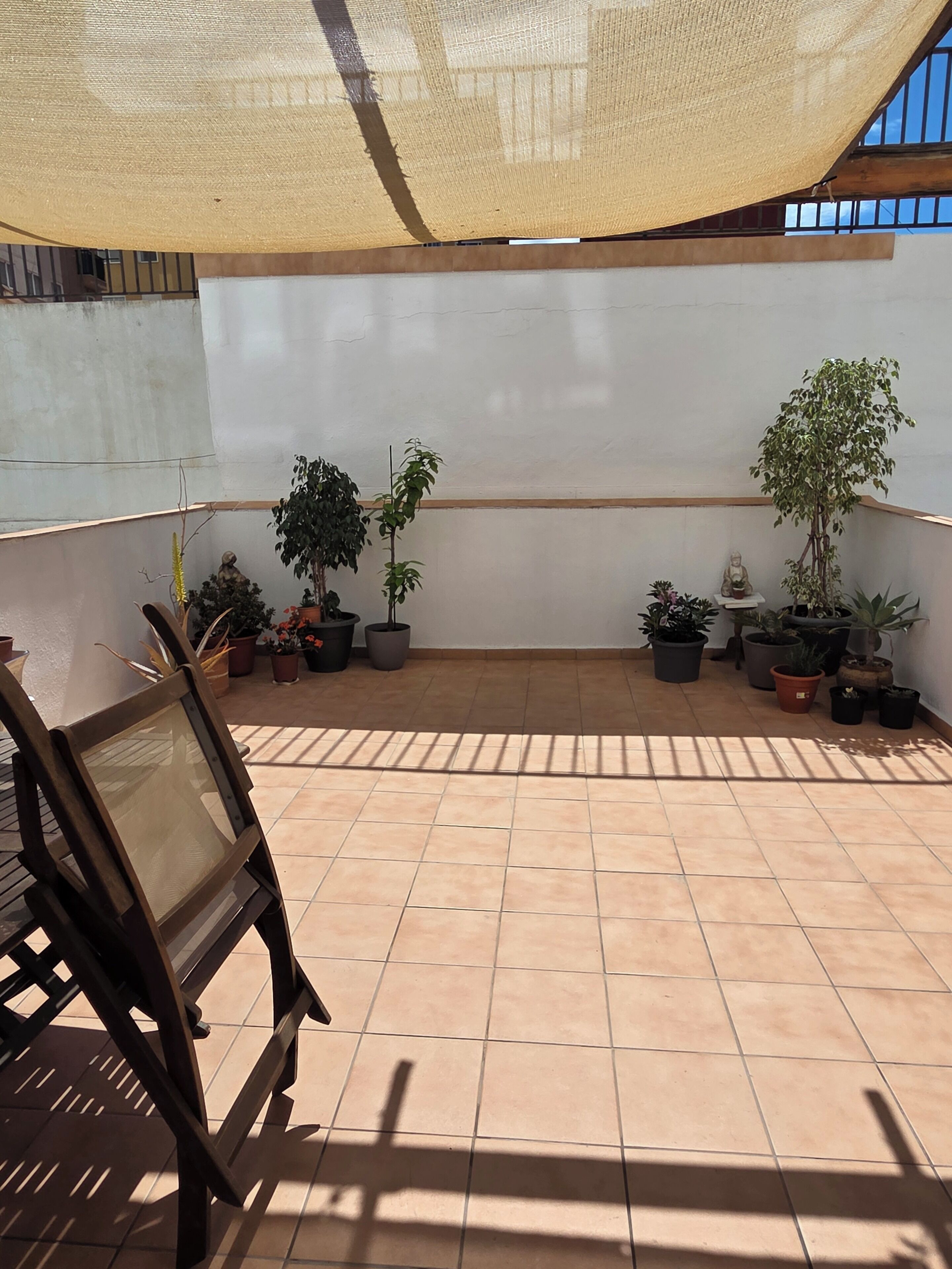 Un patio couvert avec un sol carrelé, plusieurs plantes en pot et une chaise en bois.