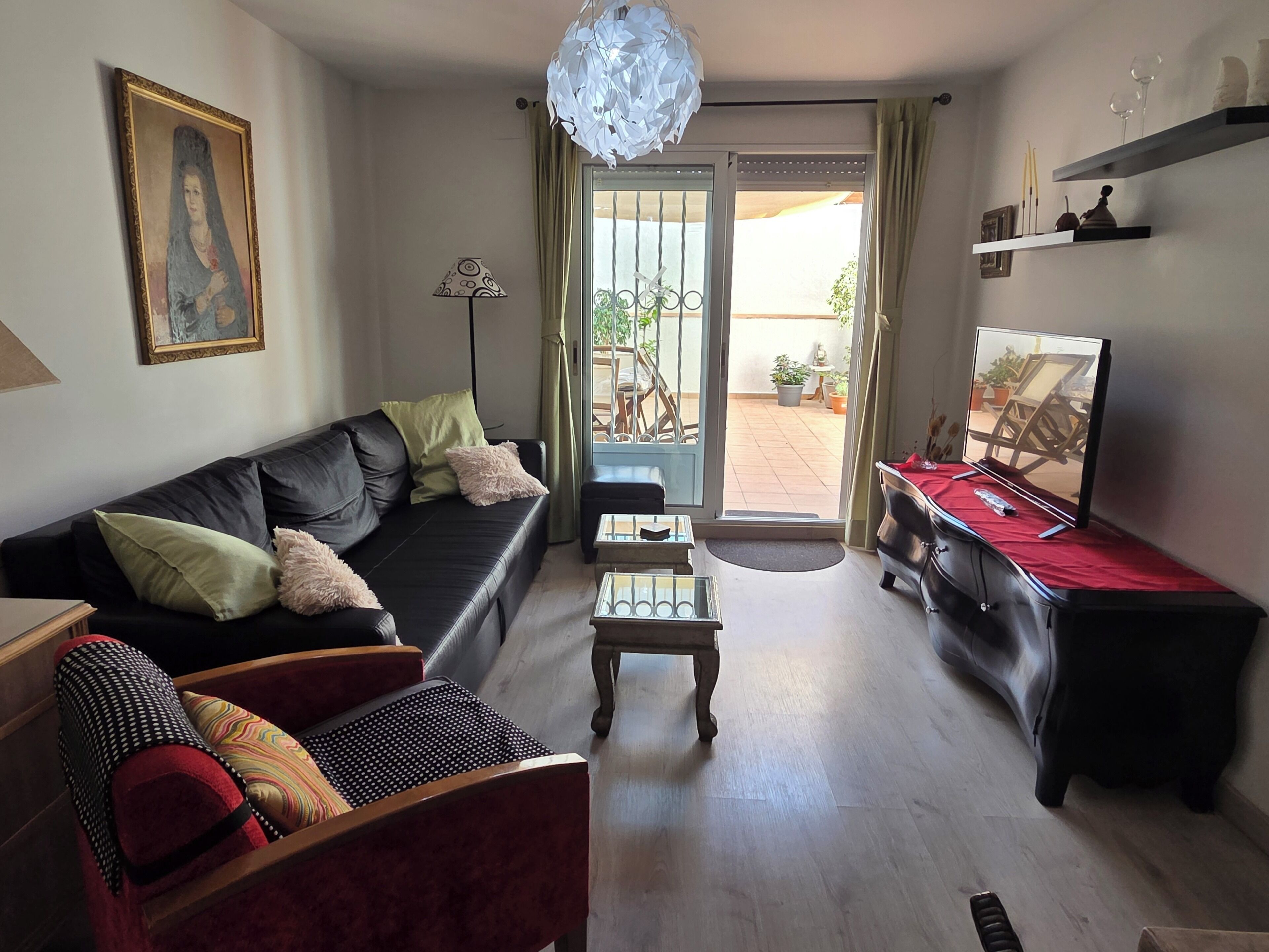 Un salon comprenant un canapé, un fauteuil, une table basse, un téléviseur et un balcon agrémenté de plantes en pot.