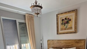 A bedroom with a large bed, a chandelier, a painting, and a view through a window with blinds. - Urban Oasis & Private Terrace. (València)