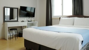 Une chambre d’hôtel avec un grand lit, un bureau doté d’un téléviseur à écran plat, un miroir et une fenêtre avec des rideaux.