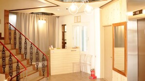 Un hall d’hôtel comprenant un comptoir d’accueil, un escalier avec des rampes rouges, un espace salon bien aménagé et un extincteur.