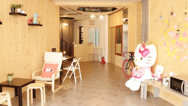 Une pièce chaleureuse aux murs en bois, ornée d’une grande décoration Hello Kitty, avec un vélo et une petite table sur laquelle se trouve un four à micro-ondes.