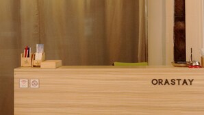 Un comptoir d’accueil avec une enseigne indiquant « ORASTAY », un comptoir en bois, un luminaire suspendu et un rideau en arrière-plan.