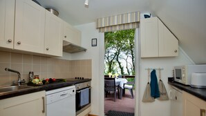 A compact kitchen with white cabinets, a built-in oven, and a microwave. There is a small dining area visible through a glass door. - Beach View - Kingsdown Resort (Kingsdown)