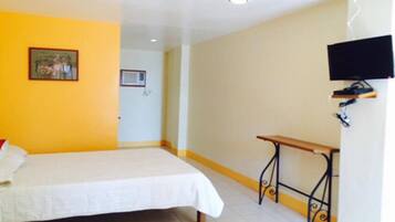 Una habitación con cama, una mesita, televisor y una puerta.