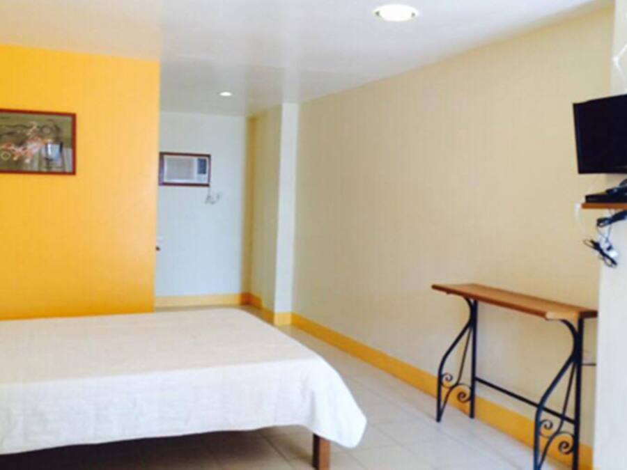 Una habitación con cama, una mesita, televisor y una puerta.