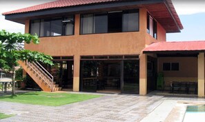 A two-story building with a covered patio area, a staircase leading to the upper floor, and a pool area. - Canoe Beach Resort (San Antonio)