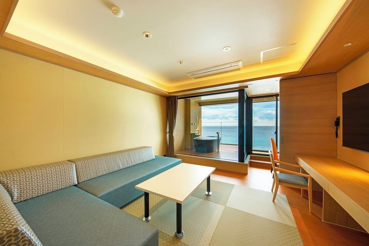 A modern room with a sofa, a small table, a TV, and a view of the sea.