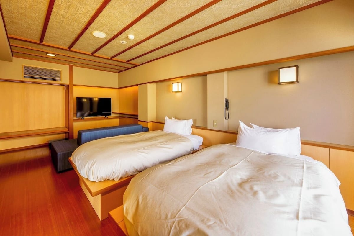 A hotel room with two beds, a TV, a bench, and a phone.