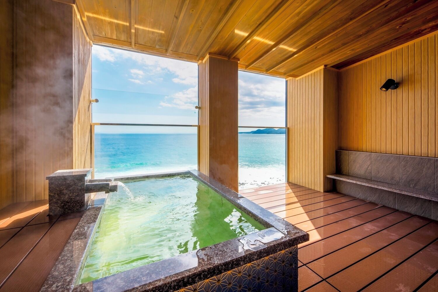 A wooden deck with a hot tub, a bench, and a view of the ocean.
