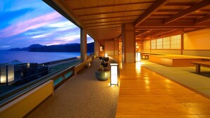 A spacious indoor area with a wooden ceiling and large windows overlooking a body of water. - Senoumi (Higashiizu)