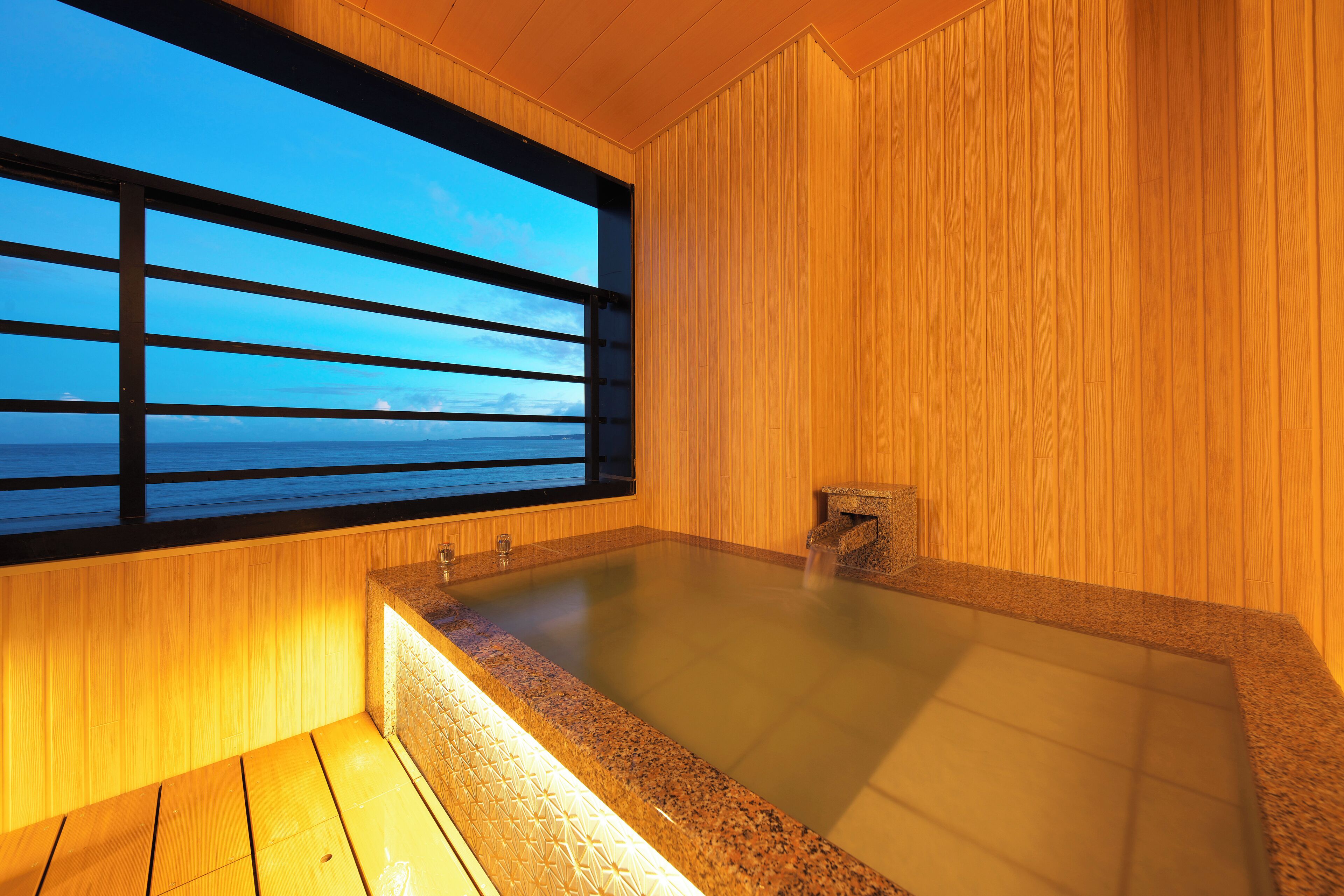 A wooden interior with a large window, a hot tub, and a stone feature.