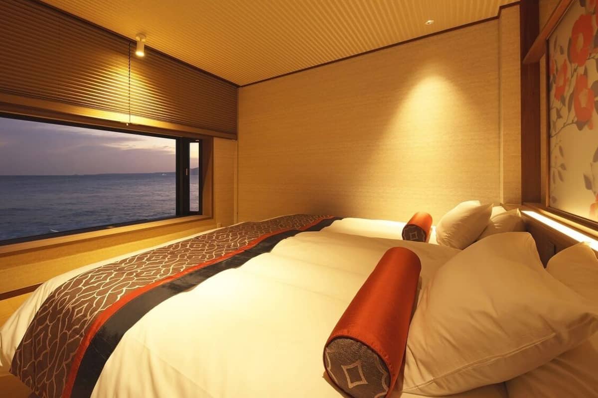 A hotel room with a large bed, a window with a view of the sea, and a decorative wall.