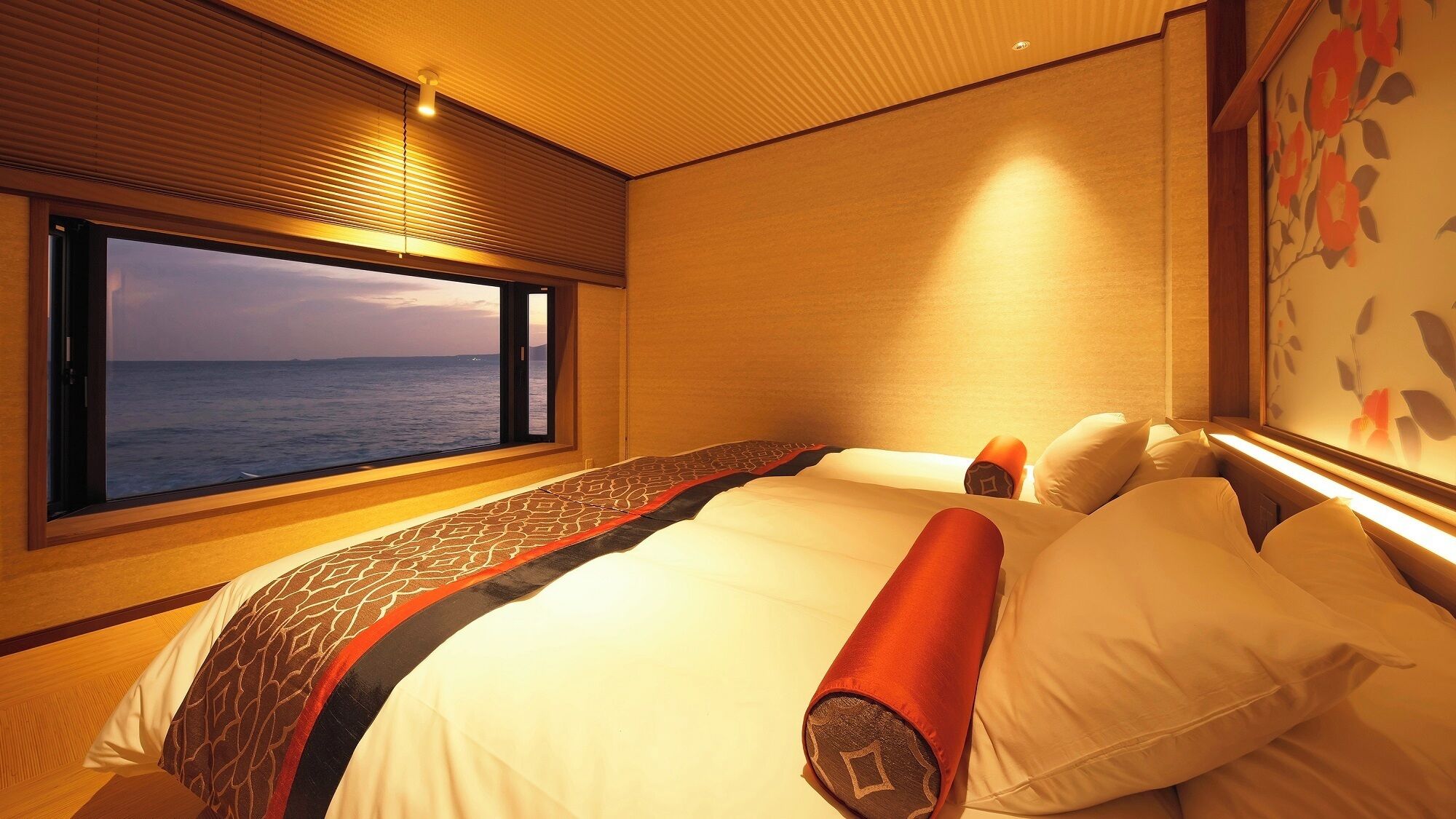 A bedroom with a large window, a bed with white bedding, and a view of the sea.